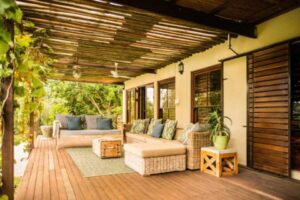 Cozy wooden patio with wicker furniture, green cushions, and potted plants.
